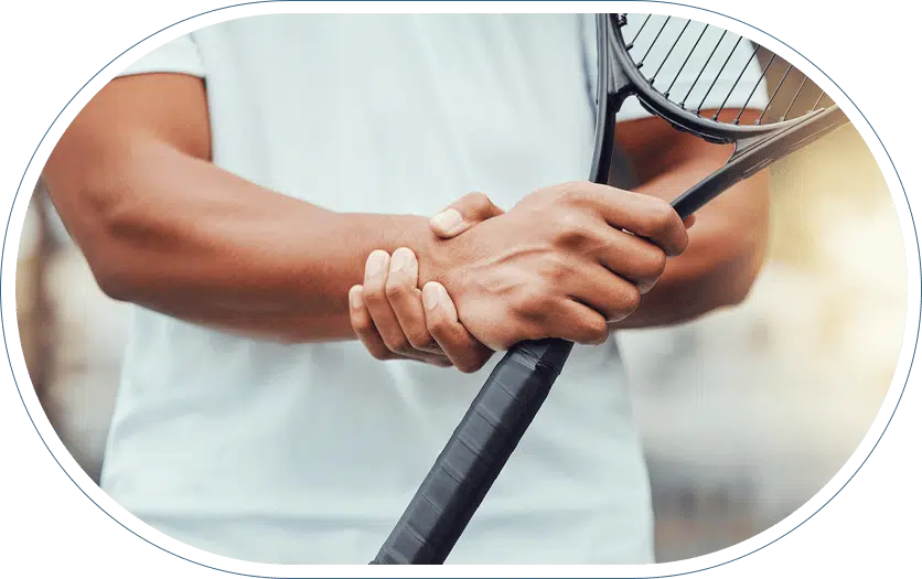 Young man holding a tennis racket in one hand and his wrist in the other in need of a pain assessment.