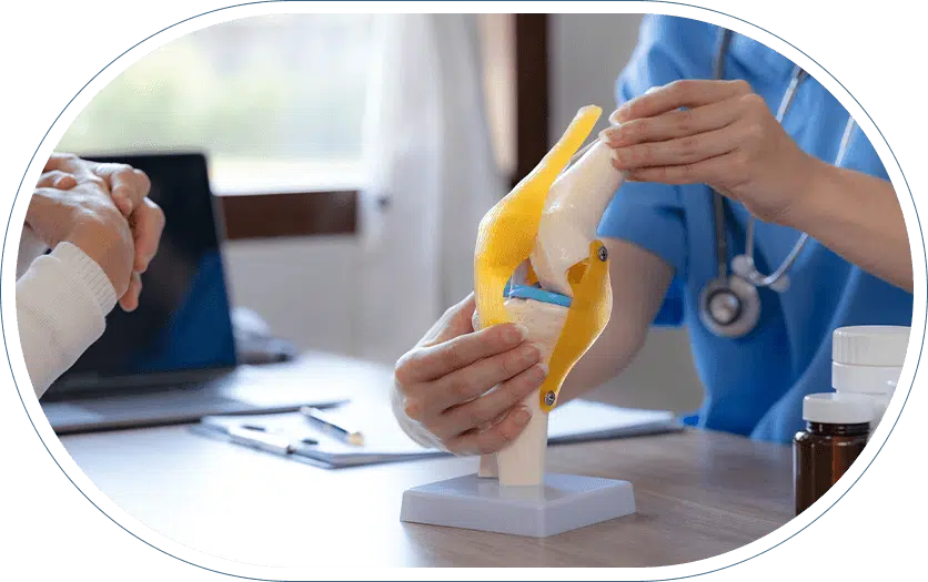 Orthopedic physician in scrubs demonstrating arthroscopic knee surgery for a meniscus tear to a patient using a model of the internal structures of the knee.