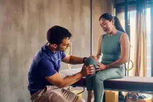Physiotherapist examining knee of female runner with knee pain.
