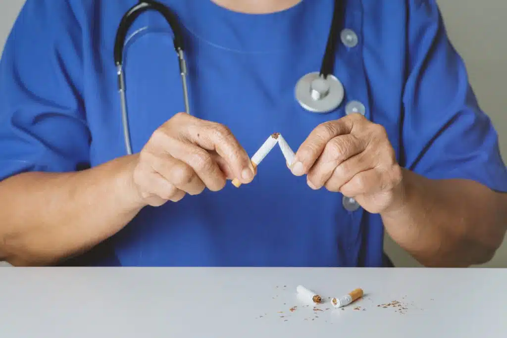 An orthopedic doctor is holding and breaking cigarette sticks with his hands on a table.