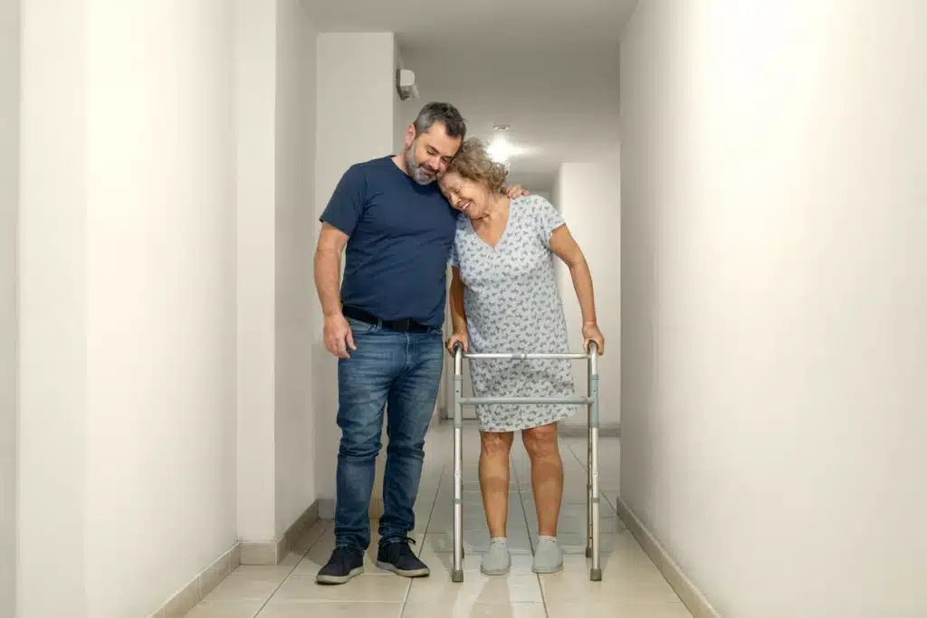 An elderly woman with a disability due to chronic hip pain is assisted by an orthopedic doctor in the hospital as she prepares for hip replacement surgery.