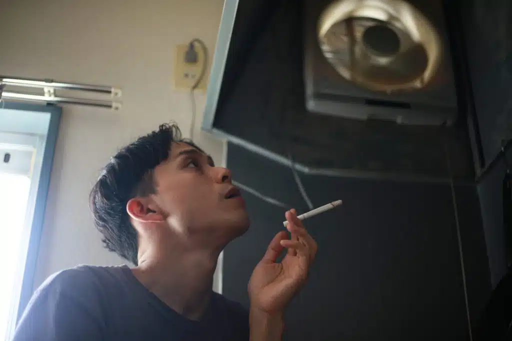 A man is smoking a cigarette beneath a ventilator before undergoing surgery.