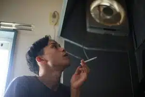 A man is smoking a cigarette beneath a ventilator before undergoing surgery.